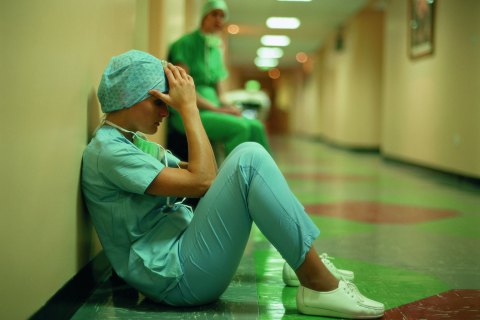 Side view of a female surgeon sitting on floor with her hand's on her head