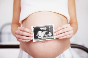 Cropped closeup of an expectant mother holding an ultrasound picture over her baby bump
